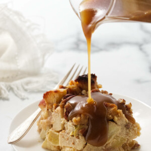 Pouring maple cream sauce over a serving of apple bread pudding.