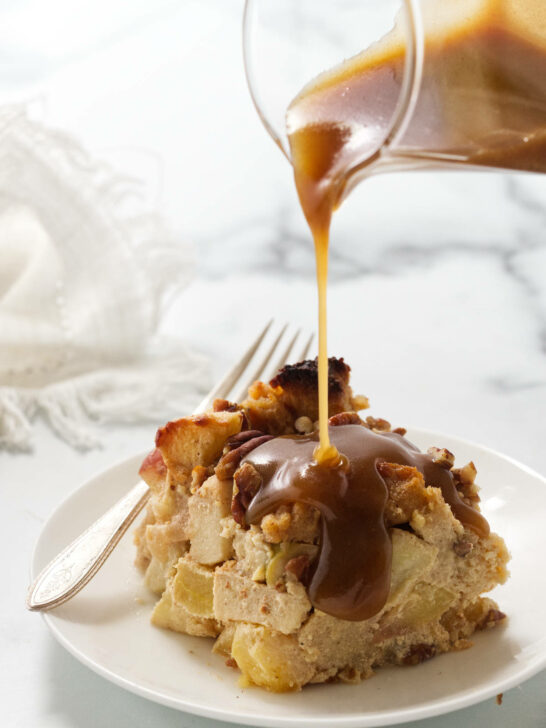 Pouring maple cream sauce over a serving of apple bread pudding.