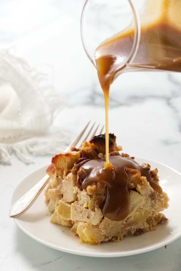 Pouring maple cream sauce over a serving of apple bread pudding.