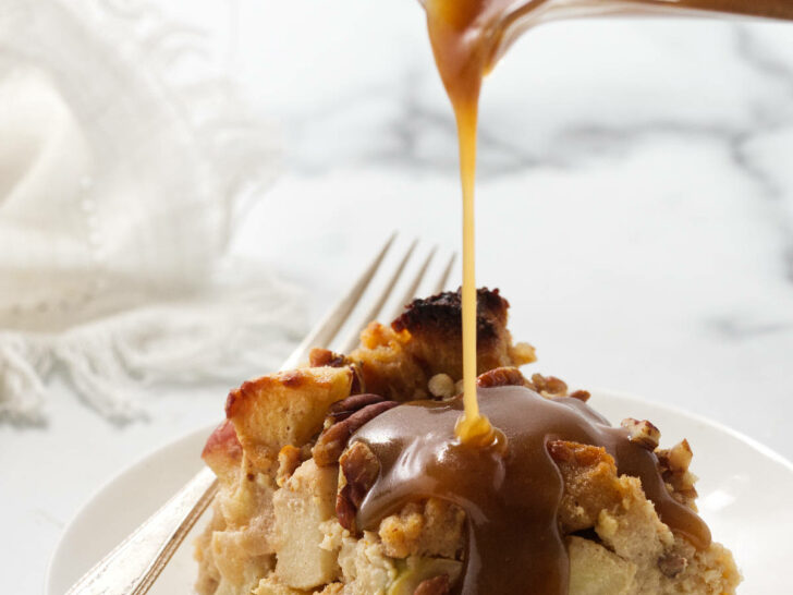 Pouring maple cream sauce over a serving of apple bread pudding.