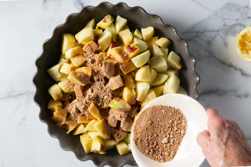 Mixing sugar and spices with sliced apples.