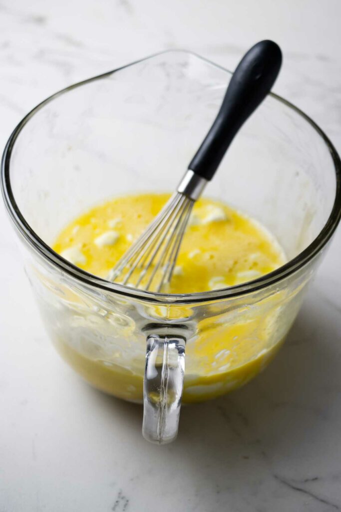 Mixing eggs and yogurt in a mixing bowl with a whisk.