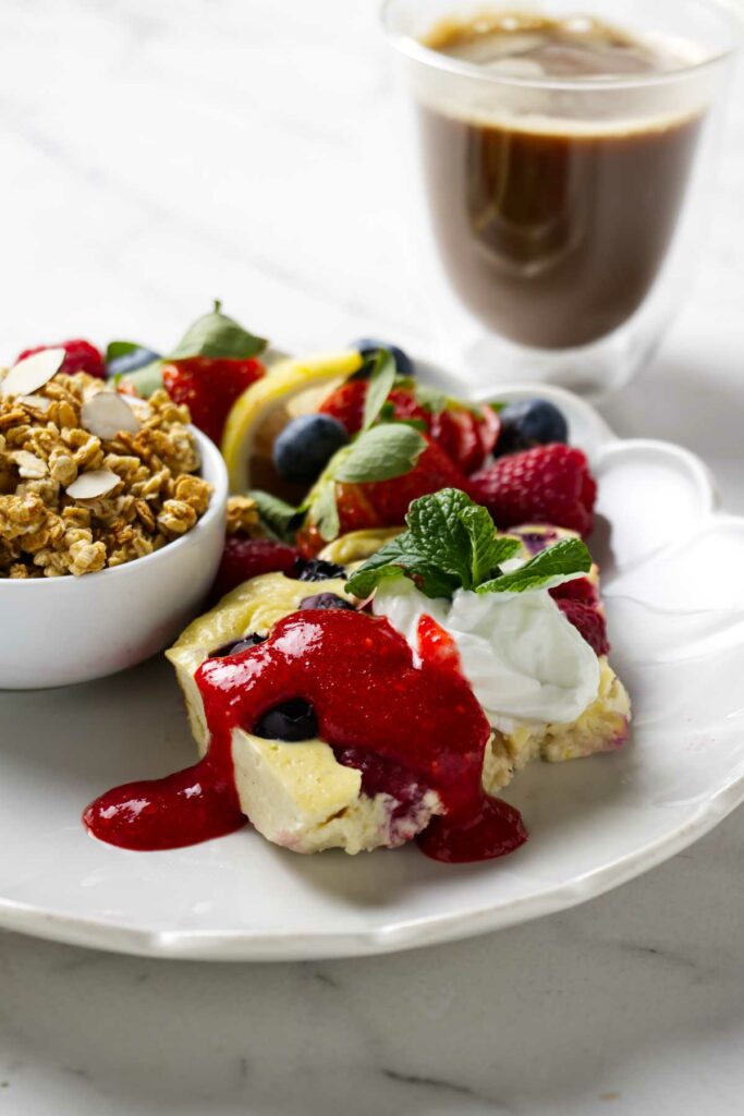 Baked yogurt custard with berries and granola and a cup of coffee in the background.