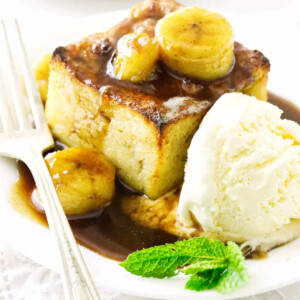 A slice of bread pudding topped with bananas and rum sauce.
