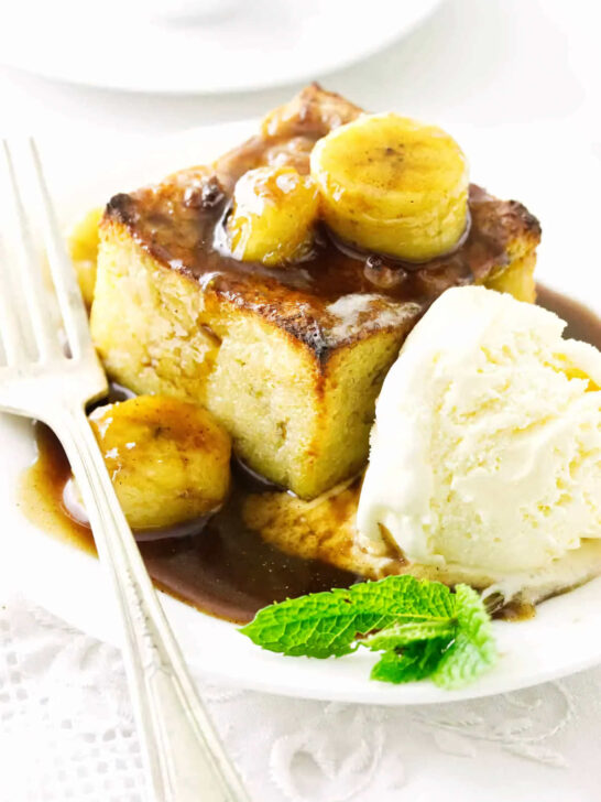 A slice of bread pudding topped with bananas and rum sauce.