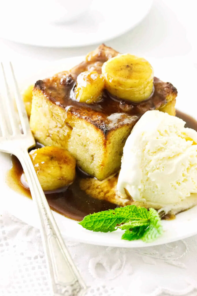 A slice of bread pudding topped with bananas and rum sauce.