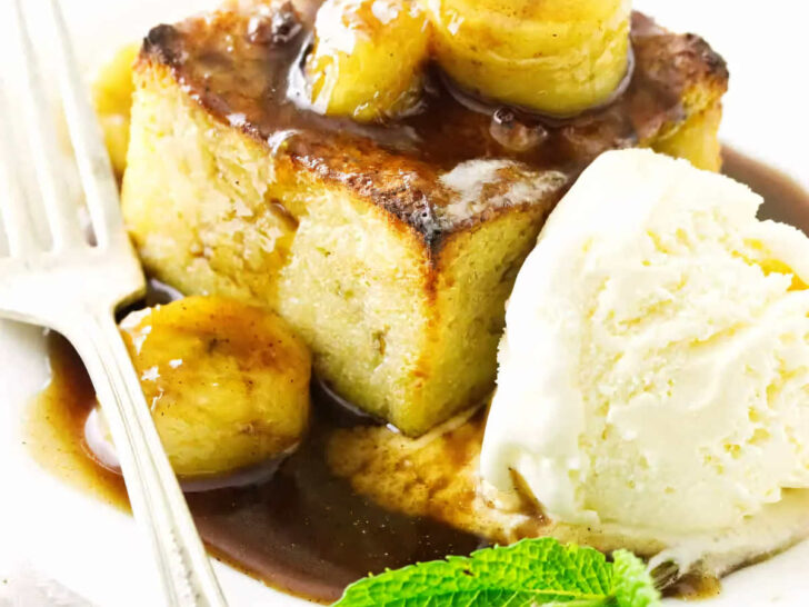 A slice of bread pudding topped with bananas and rum sauce.