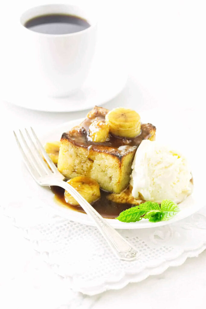 A cup of coffee next to a serving of bread pudding topped with bananas and rum sauce.