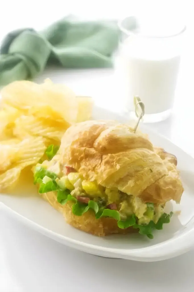 A plate with a curried chicken sandwich next to a glass of milk.