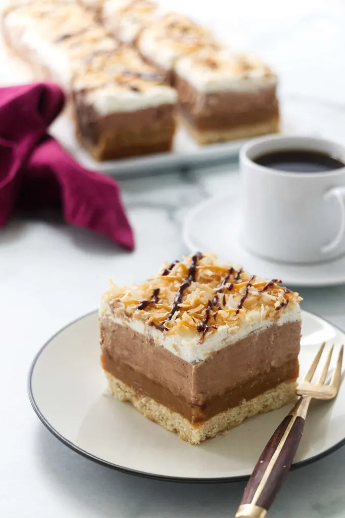 A serving of a samoa dessert lasagna with a cup of coffee in the background.