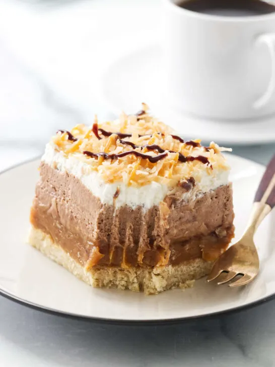 A partially eaten no bake chocolate coconut caramel cheesecake bar next to a cup of coffee.