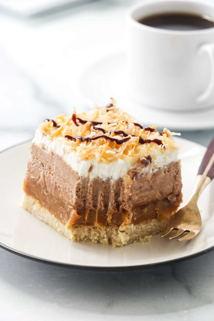 A partially eaten no bake chocolate coconut caramel cheesecake bar next to a cup of coffee.