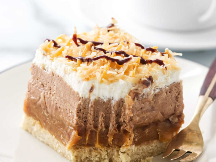 A partially eaten no bake chocolate coconut caramel cheesecake bar next to a cup of coffee.