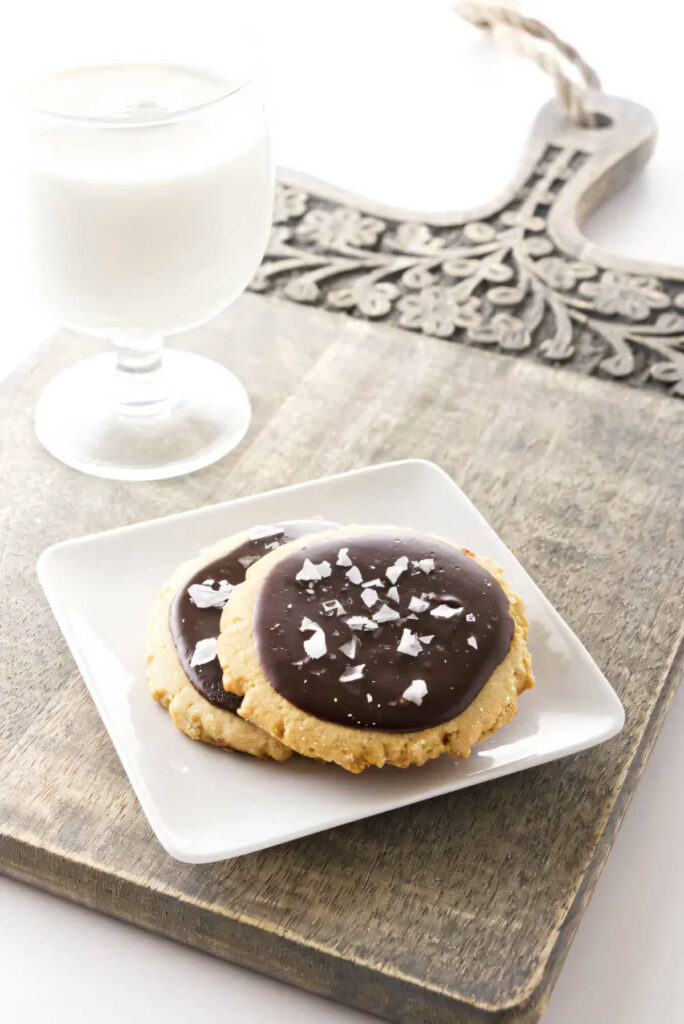 Two cookies on a dessert plate next to a glass of milk.