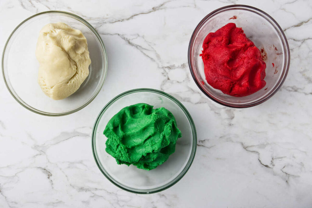 Three bowls filled with cookie dough, each colored with red, green, and white.