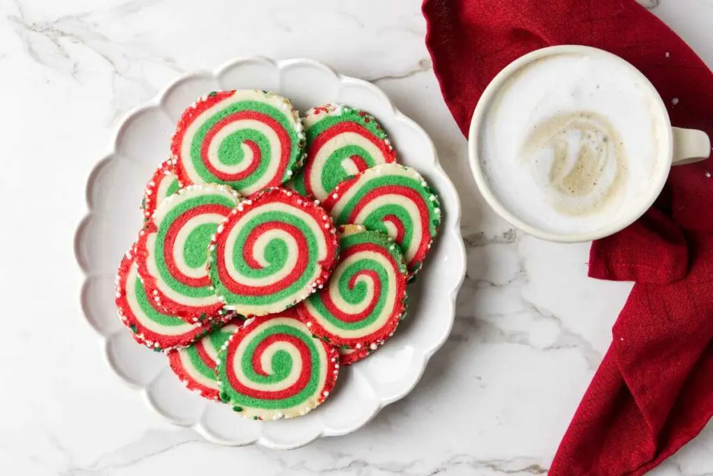 A plate of red and green swirled cookies next to a cup of coffee. 