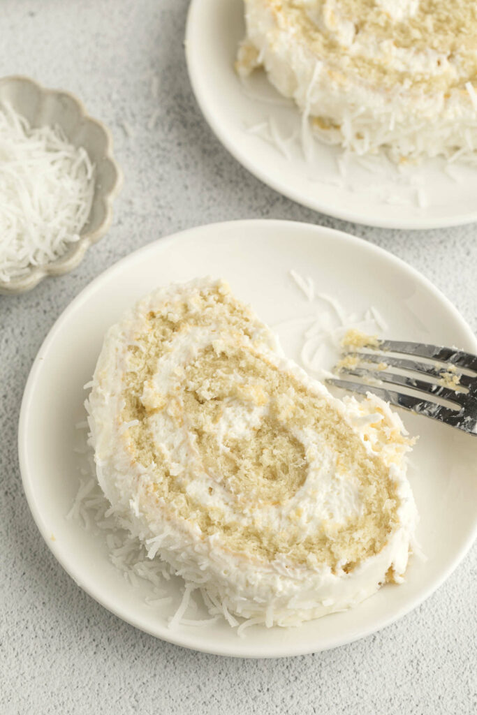 A fork on a plate with a slice of rolled coconut cake.