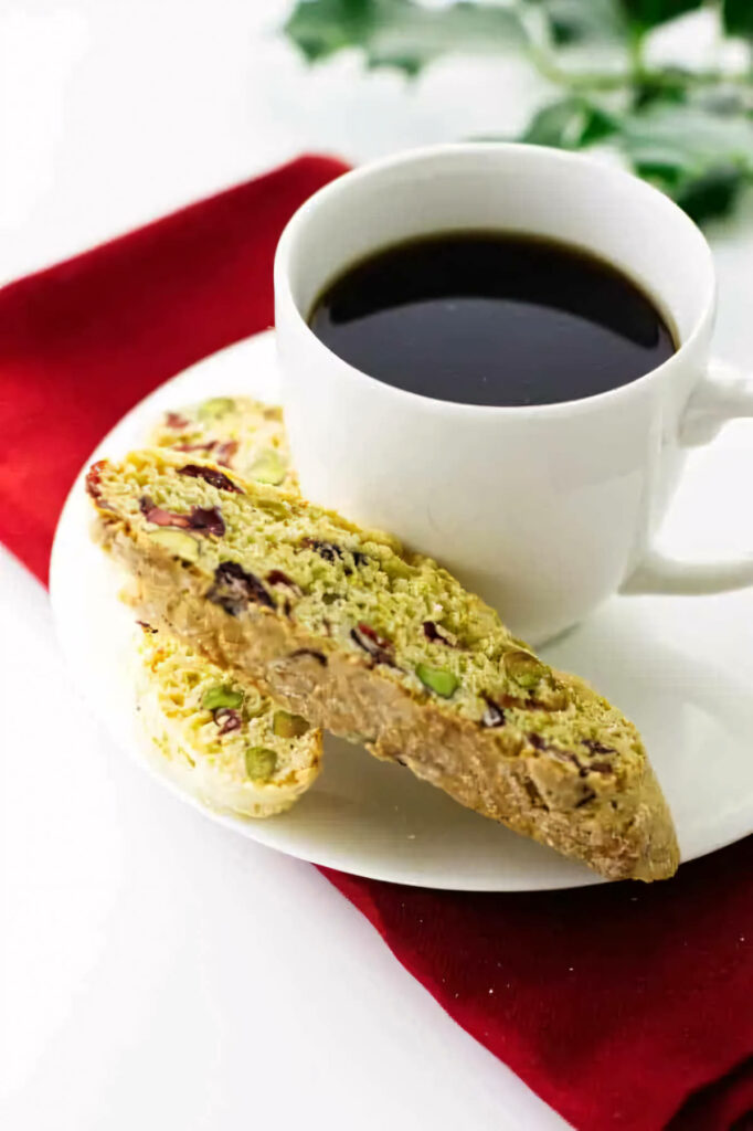 Two cranberry and pistachio biscotti on a plate with a cup of coffee.