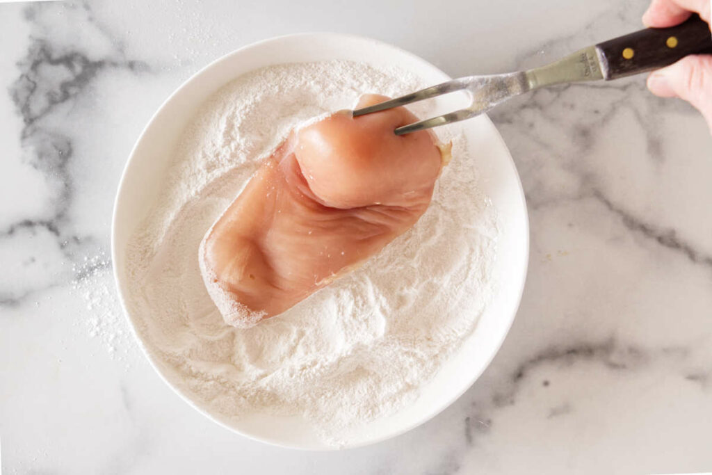 Coating a chicken breast in flour.