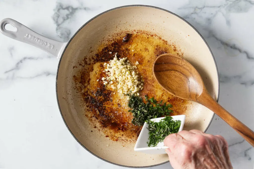 Adding garlic and herbs to a skillet.