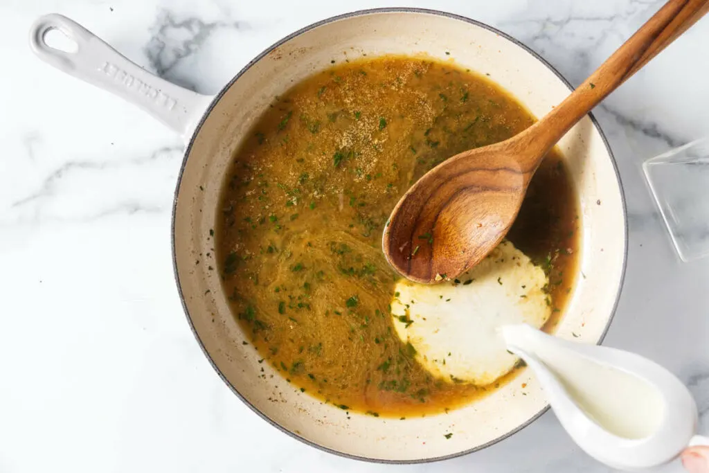 Stirring cream into the skillet to make a creamy sauce.