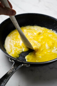 Pushing scrambled eggs aside in a pan to make a cheese omelette.