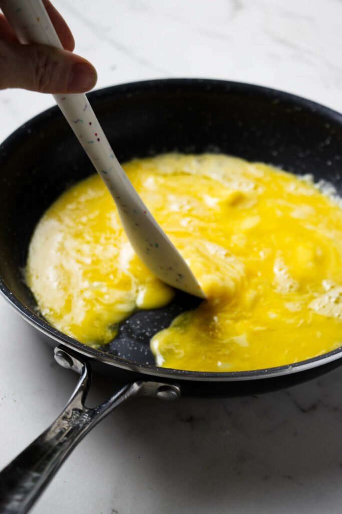 Pushing scrambled eggs aside in a pan to make an omelette.