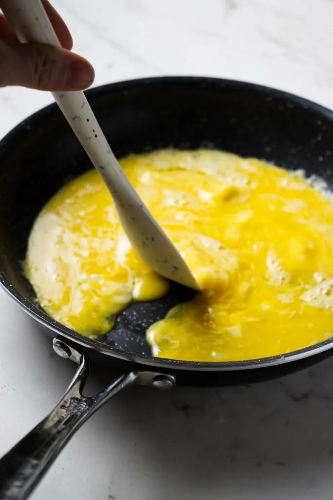 Pushing scrambled eggs aside in a pan to make an omelette.