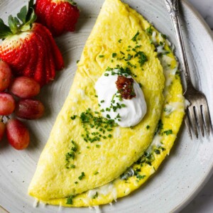 A cheese omelet on a plate with fruit and a dollop of sour cream.