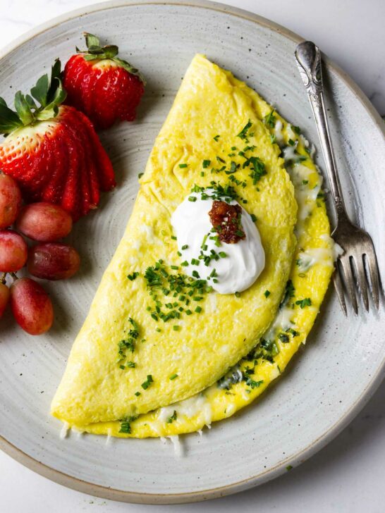 A cheese omelet on a plate with fruit and a dollop of sour cream.