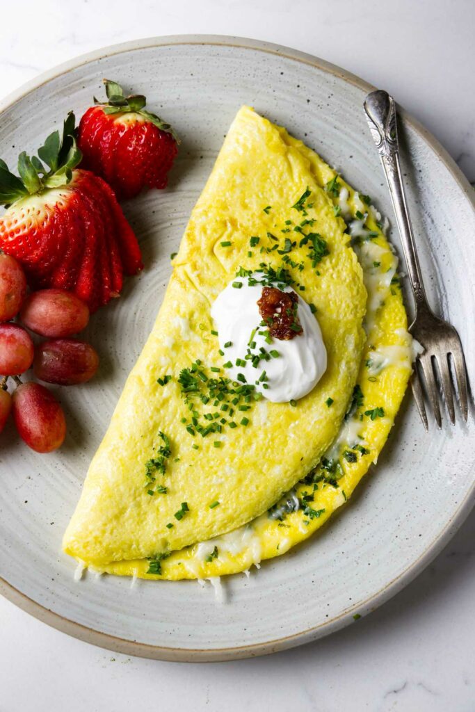 A cheese omelet on a plate with fruit and a dollop of sour cream.