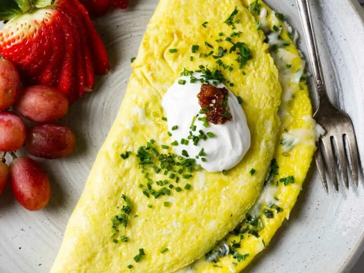 A cheese omelet on a plate with fruit and a dollop of sour cream.