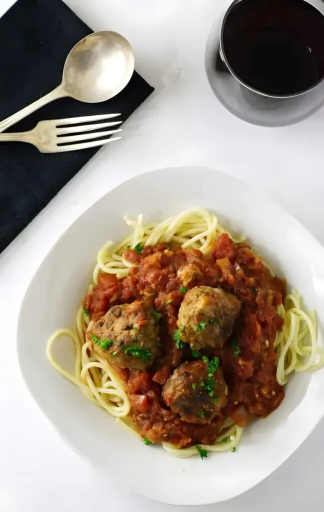 A plate of spaghetti and meatballs next to a glass of red wine.