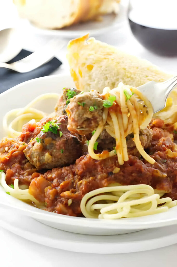 A fork with a bite of meatball and noodles with red sauce.