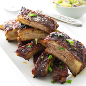 A platter filled with slices of Asian sticky pork ribs with kimchi in the background.