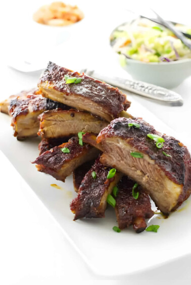 A platter filled with slices of Asian sticky pork ribs with kimchi in the background.