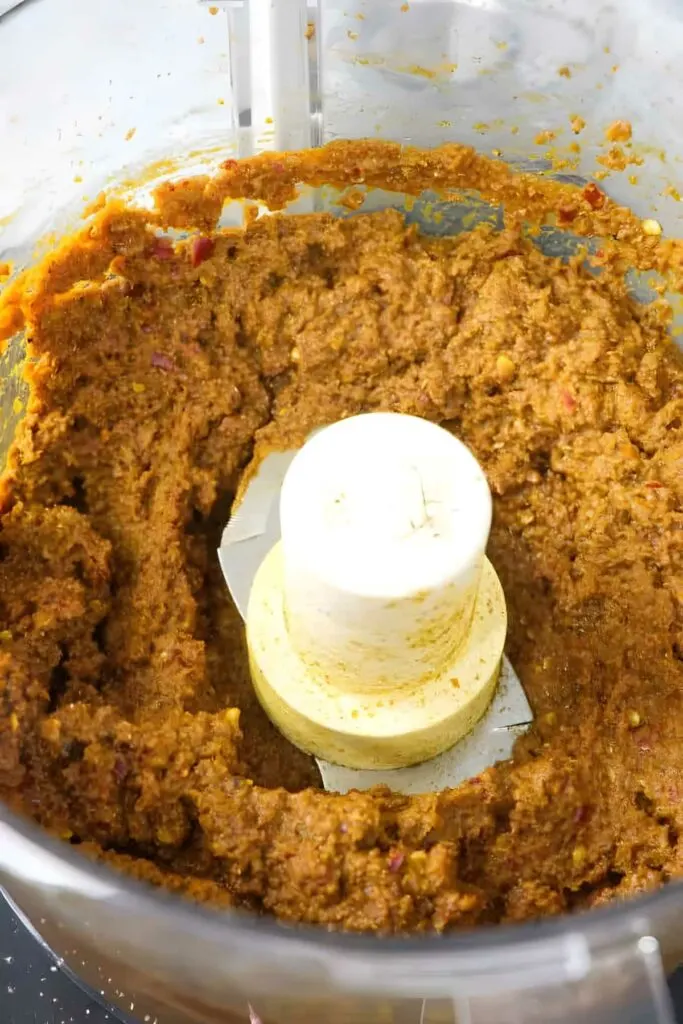 Blending curry, chili, and fresh herbs in a food processor bowl.