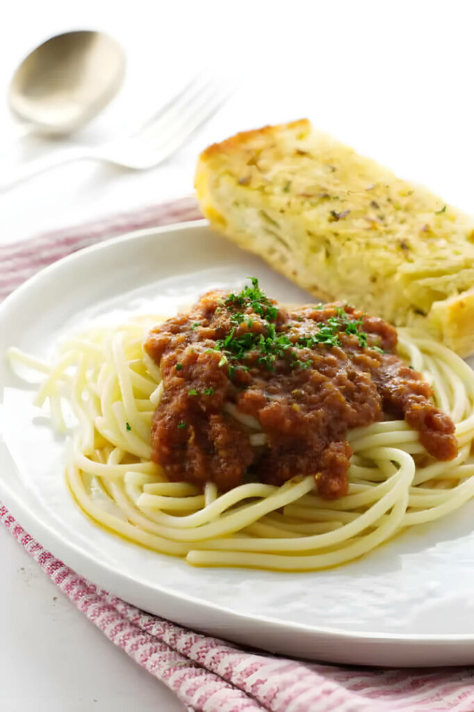 Red pasta sauce on a pile of spaghetti noodles next to a slice of garlic bread.