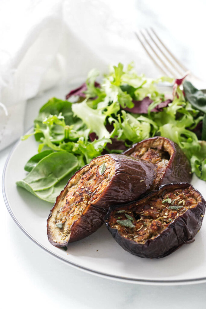 Slices of oven baked eggplant on a plate with a green salad.