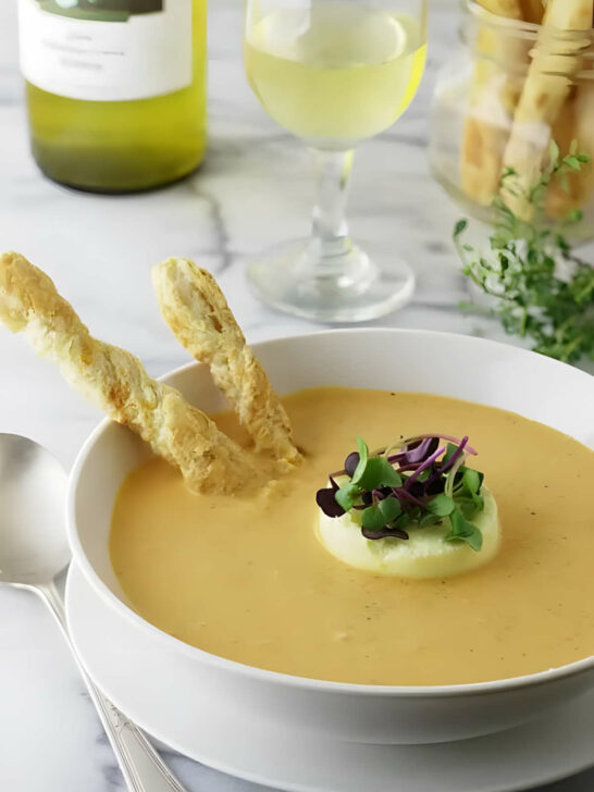 A bowl fill with creamy roasted garlic tomato soup with bread sticks and cheese flan.