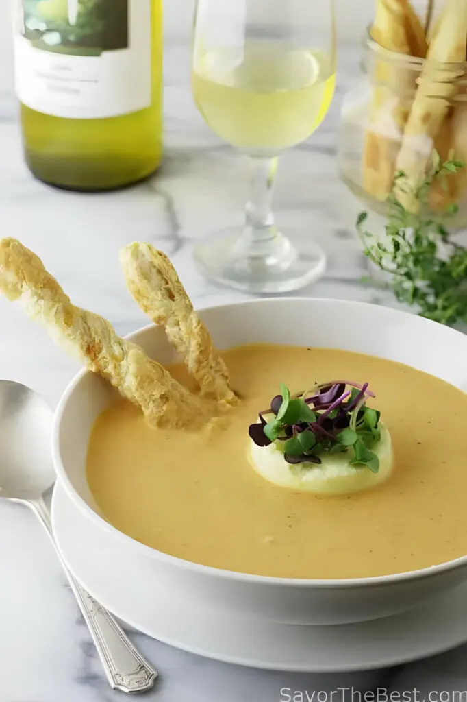 A bowl fill with creamy roasted garlic tomato soup with bread sticks and cheese flan.