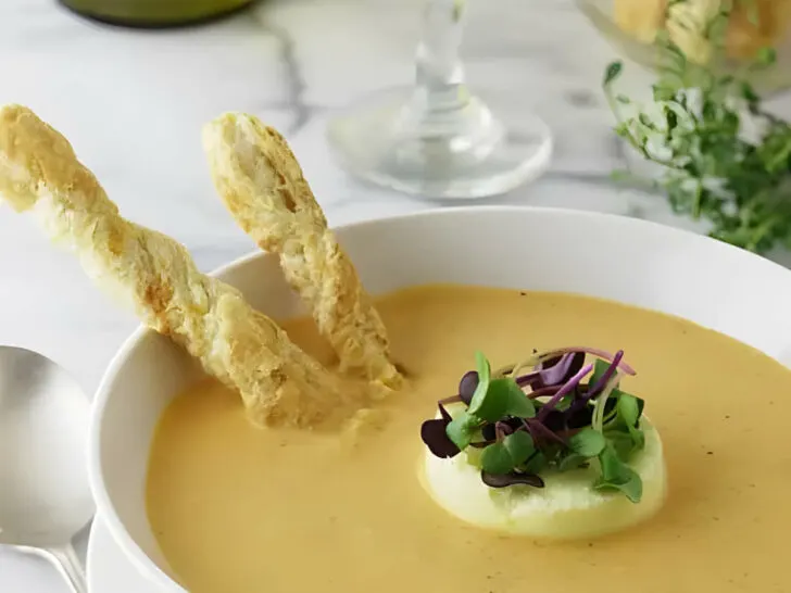 A bowl fill with creamy roasted garlic tomato soup with bread sticks and cheese flan.