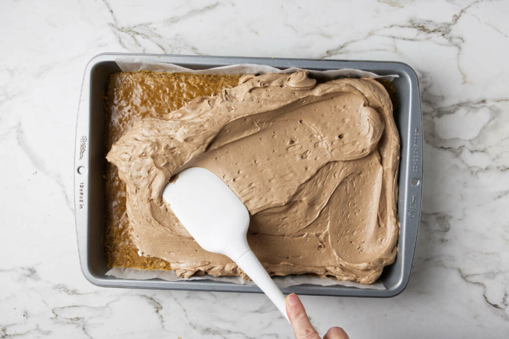 Spreading a chocolate cheesecake mixture over a layer of caramel on a shortbread crust.