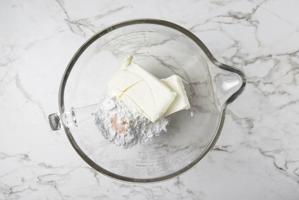 Combining sugar and cream cheese in a mixing bowl.