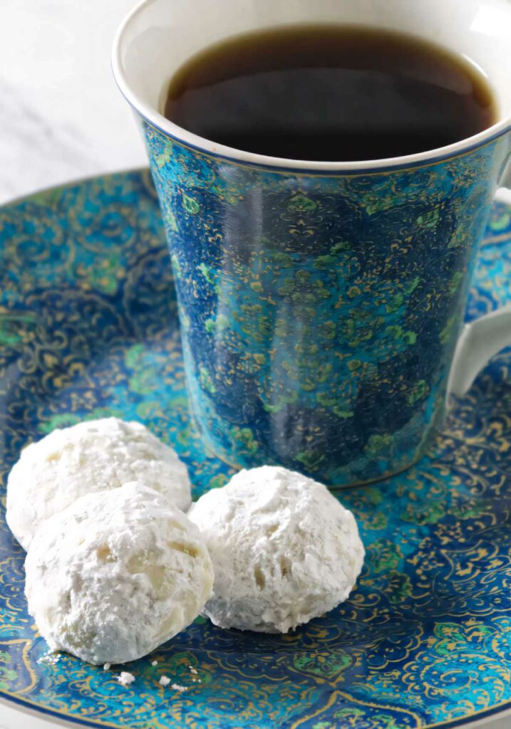 Three snowball cookies on a plate with a cup of coffee.