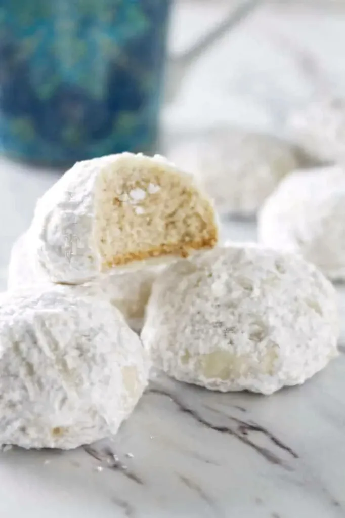 A partially eaten cookie on a stack of more snowball cookies.