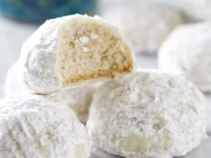 A partially eaten cookie on a stack of more snowball cookies.