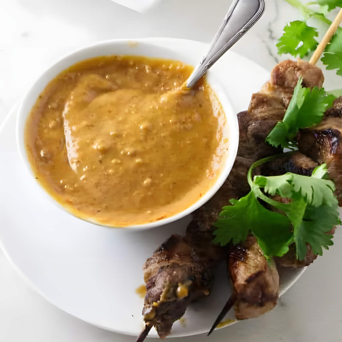 A small dish of peanut sauce next to some chicken kabobs.