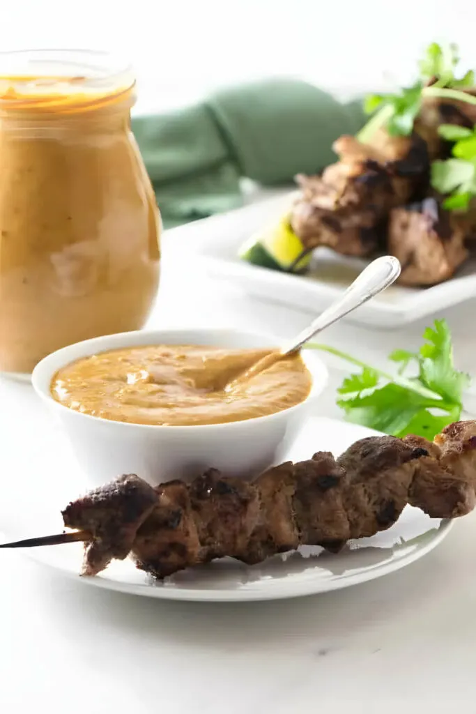 An appetizer plate with chicken and peanut sauce along with a jar of sauce in the background.