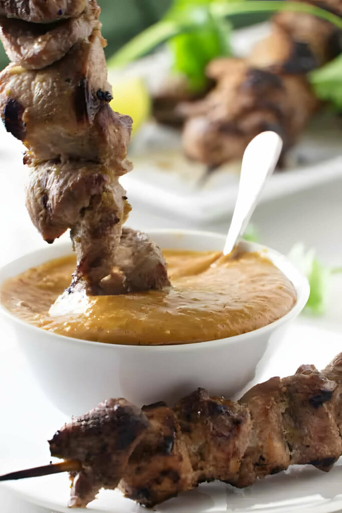 Dipping chicken into a dish of creamy peanut sauce.